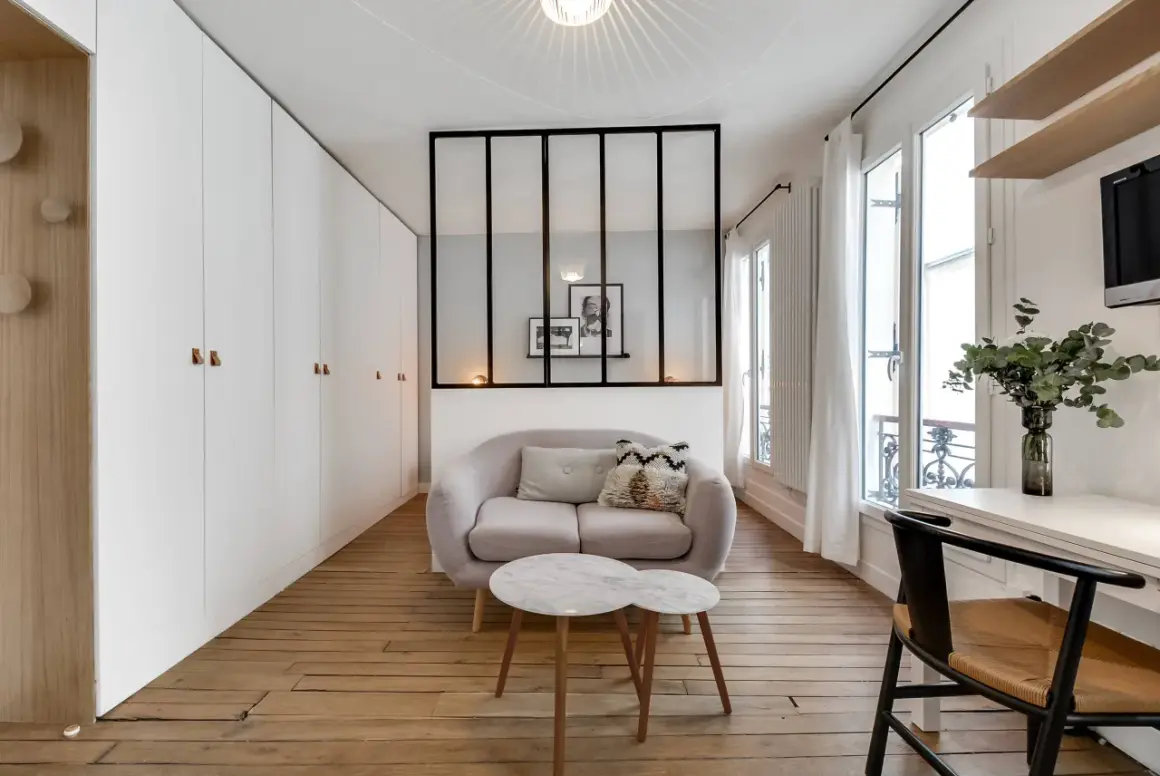 Ein moderner Raumteiler mit schwarzen Metallstreben trennt den Wohnbereich mit einem Sofa und Couchtisch vom Rest des Zimmers.