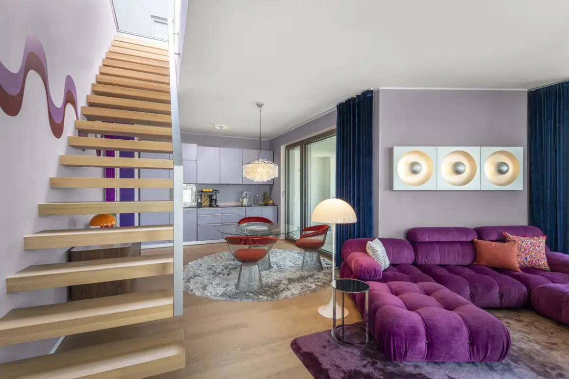 Ein Wohnbereich im 70er jahre einrichtungsstil mit lila Sofa, runden roten Stühlen und einer Holztreppe.
