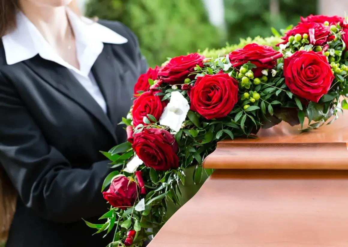 Osoba w czerni kładzie wieniec pogrzebowy z czerwonych róż na trumnie. Wieniec pogrzebowy znaczenie to symbol miłości i pamięci.