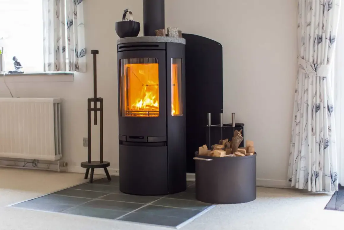 Ein moderner schwarzer Kamin mit brennendem Feuer. Daneben ein Korb mit Holzscheiten, bereit für den Kamin zug.