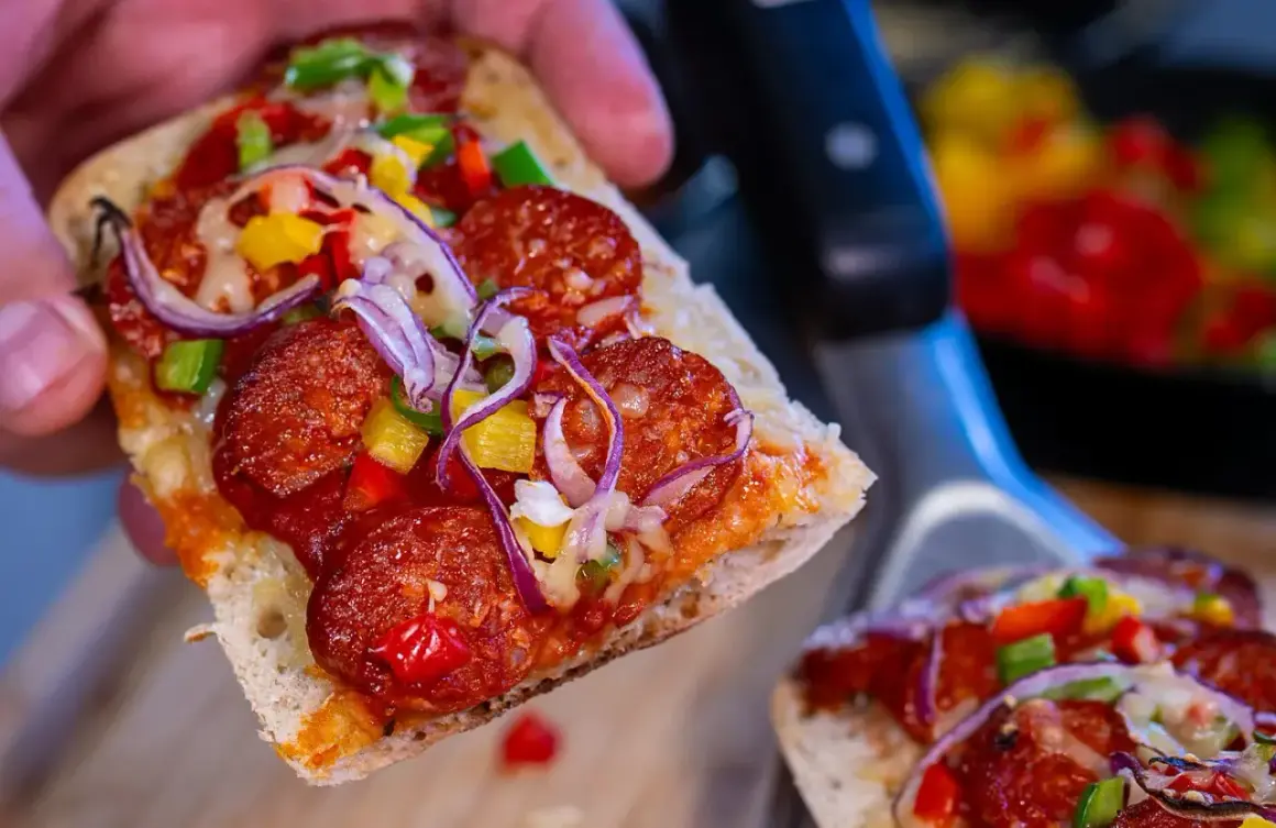 Pyszna zapiekanka z chorizo, papryką i cebulą, trzymana w dłoni.