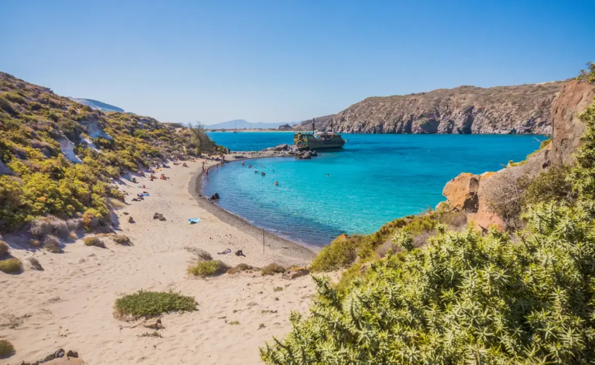 Piękna plaża na wyspie Nisyros z turkusową wodą, łodzią i ludźmi odpoczywającymi na piasku.