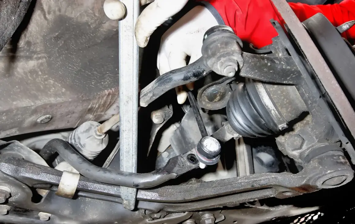 Montaż łącznika stabilizatora Toyota Yaris 1. Widoczna ręka w rękawiczce przykręca element zawieszenia.