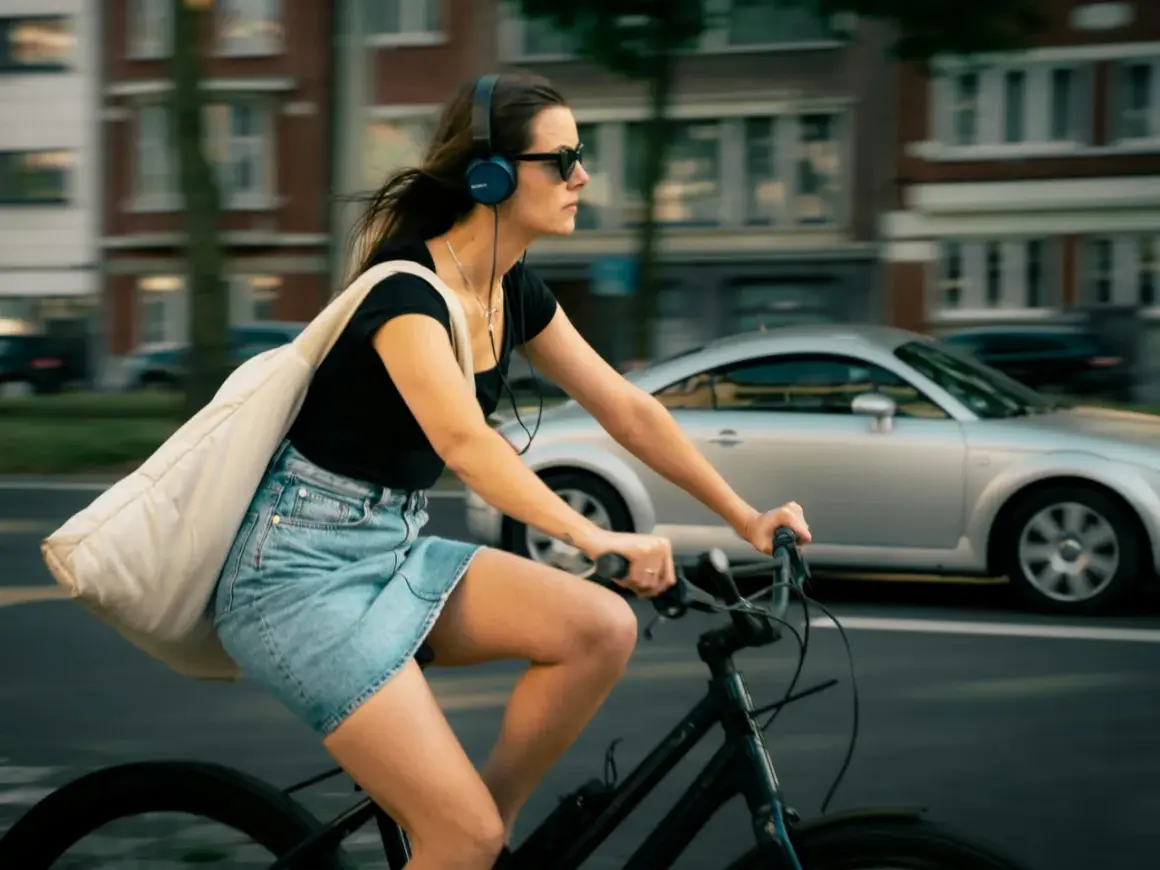 Frau fährt Fahrrad mit Kopfhörern und Tasche. Ob man mit AirPods Fahrrad fahren darf, ist eine Frage der Sicherheit und des Gehörs.