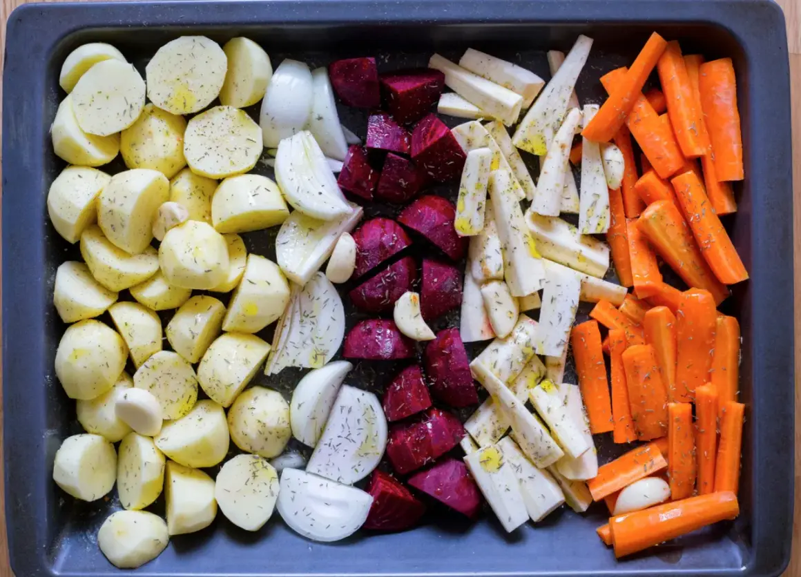 Ugnsrostade rotfrukter: potatis, morötter, palsternacka, rödbetor och lök, kryddade och redo för ugnen.