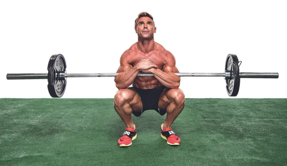 Muskulös man utför en zercher squat med skivstång i armvecken.
