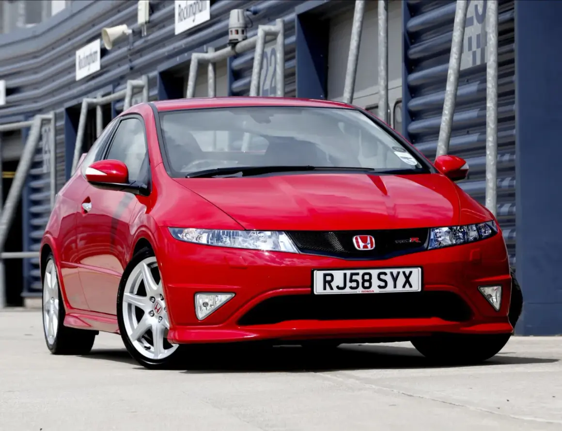 Czerwony Honda Civic Type R, wyglądający jak futurystyczne UFO, zaparkowany na torze wyścigowym.