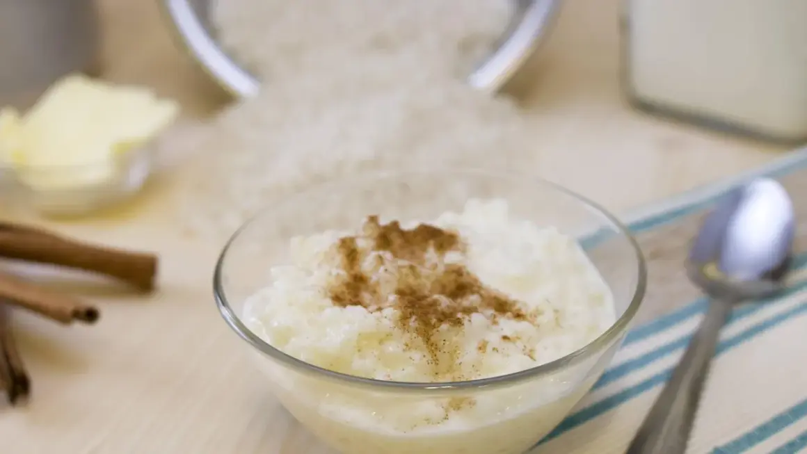 Schüssel mit Milchreis, Zimt, Butter, Zimtstangen und Reis. Die Frage, wie lange ist Milchreis nach MHD haltbar, beschäftigt viele.