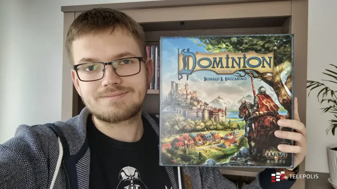 Uśmiechnięty mężczyzna prezentuje pudełko gry "Dominion II Edycja". To dopiero początek przygody z nowymi dodatkami!