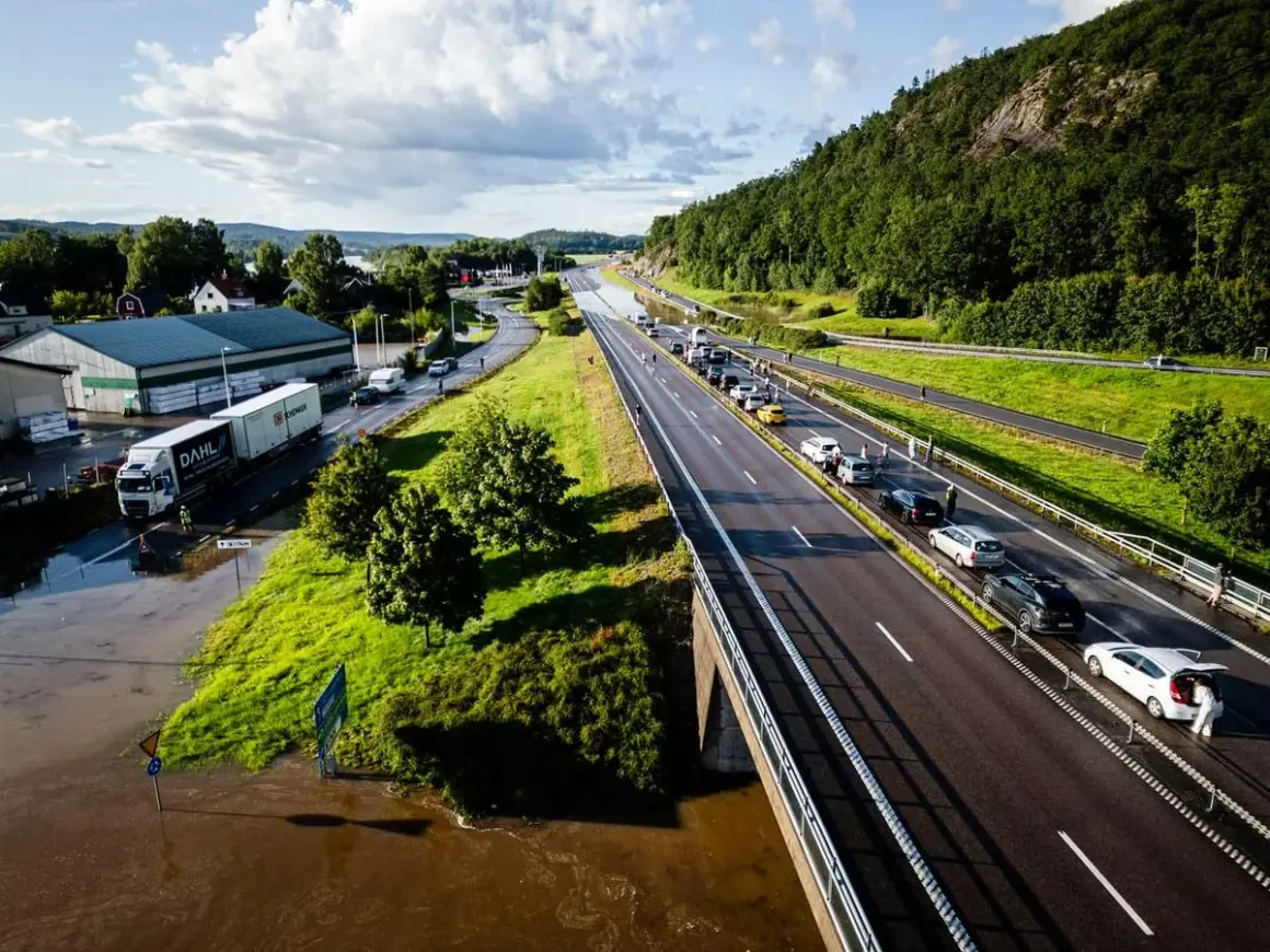 Trafikkaos vid en översvämmad rastplats. Bilar står stilla på motorvägen, en lastbil har fastnat i vattnet.
