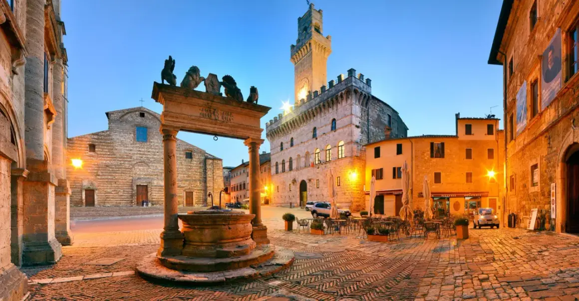 Piazza illuminata a Montepulciano, con pozzo rinascimentale, Palazzo Comunale e chiese. Perfetta per scoprire le cose da fare in zona.