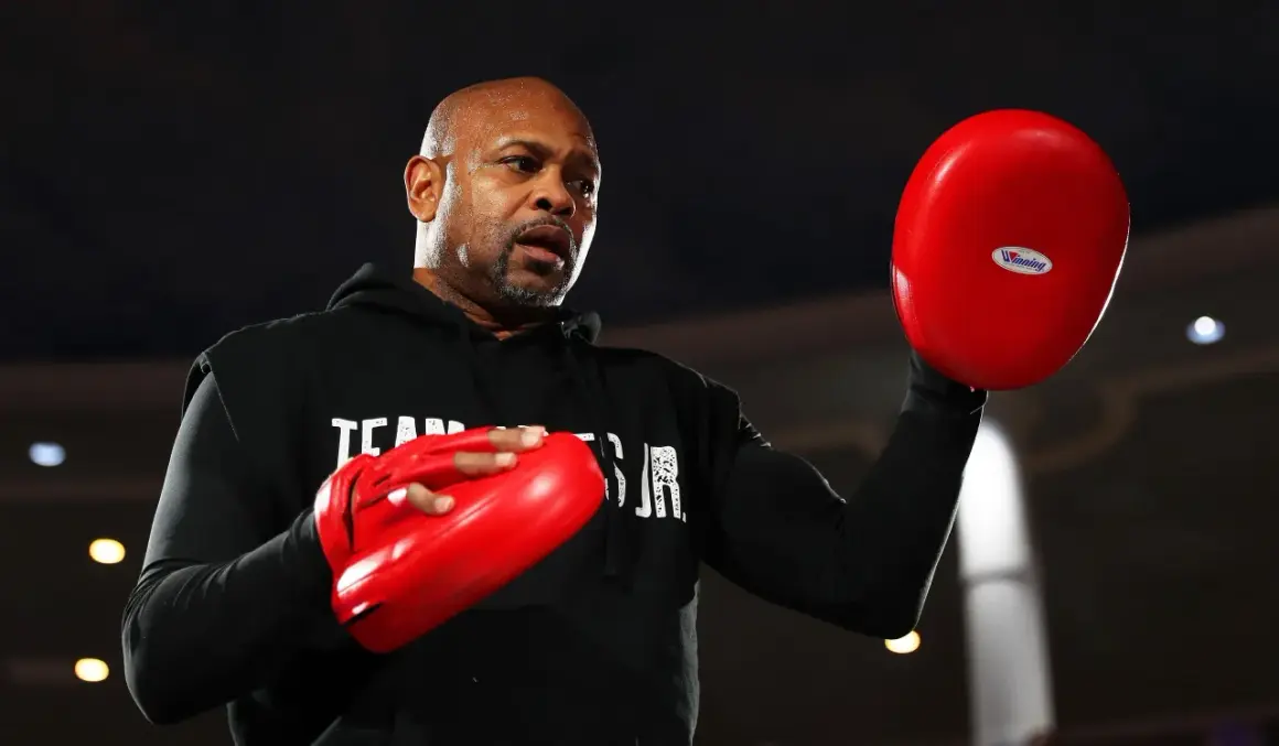 Roy Jones Jr. sweats during training, preparing for one of his best fights. He holds red boxing pads, ready to train.