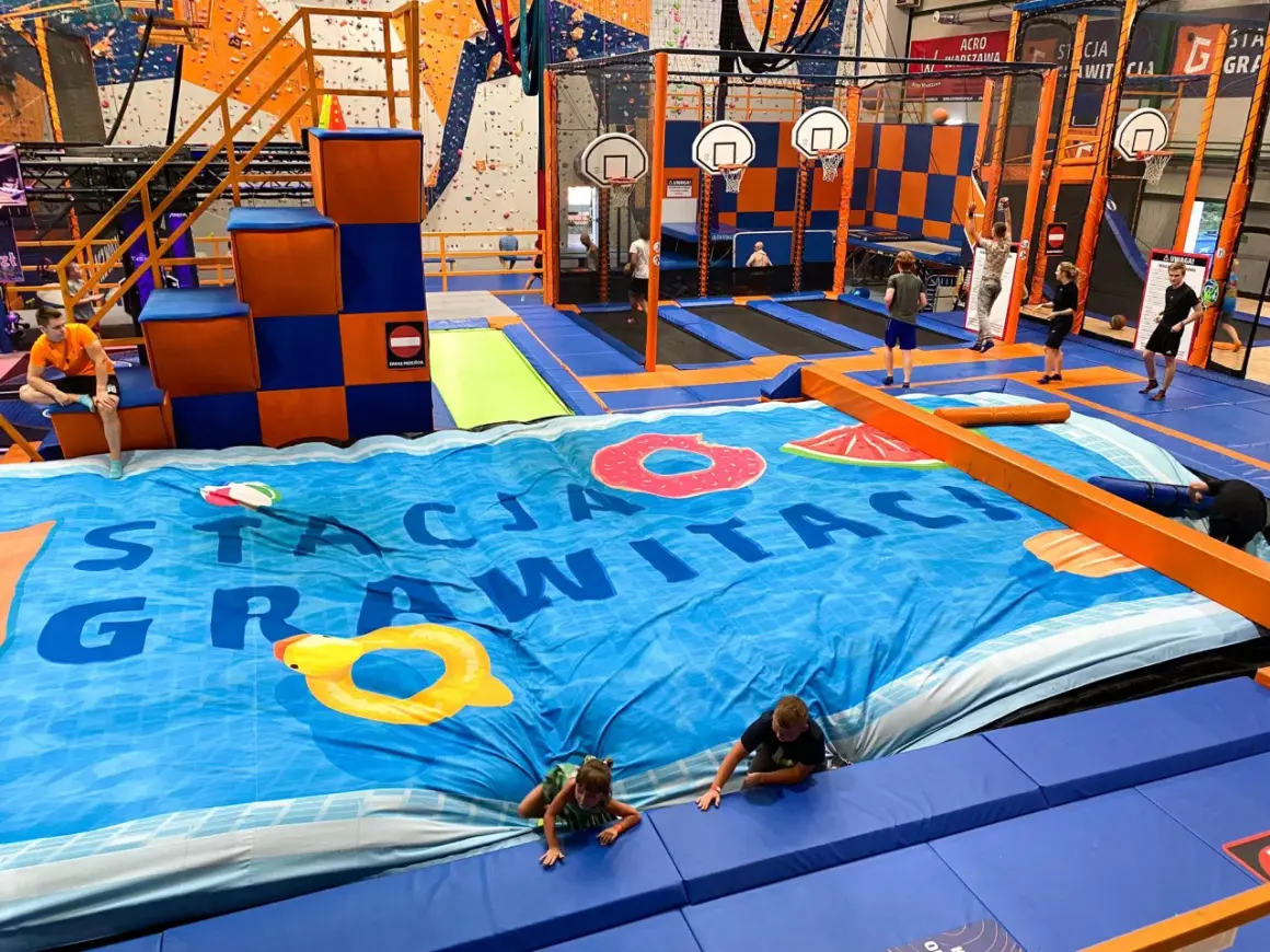 Wesołe skakanie na trampolinach w centrum rozrywki dla dorosłych. Dzieci i młodzież bawią się na wielkiej, niebieskiej macie z motywem basenu.