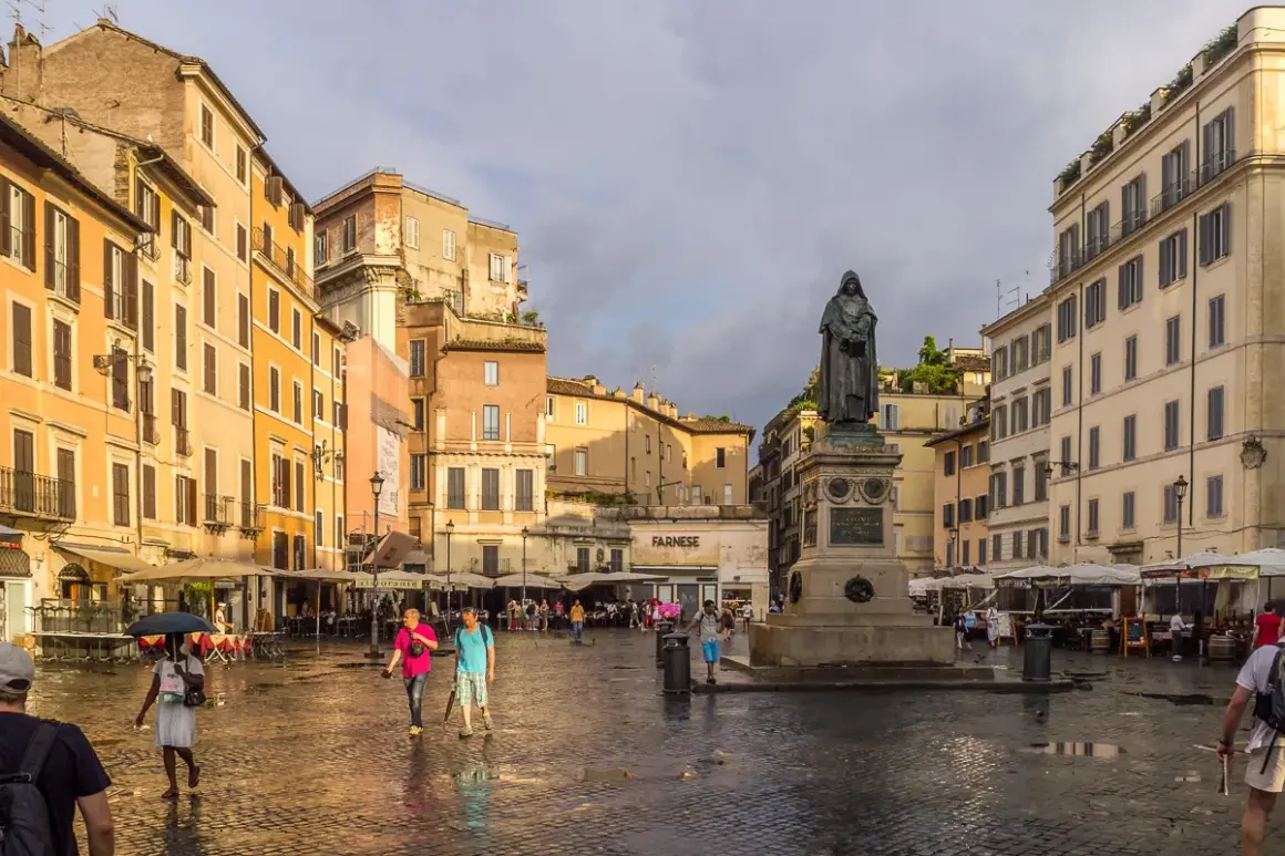 Campo de' Fiori, Rzym. Po deszczu, na mokrym bruku placu, ludzie spacerują obok pomnika.