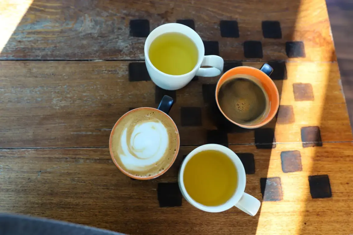 Kawa i herbata na drewnianym stole. Czy zielona herbata pobudza? Obok kawy latte i espresso, dwie filiżanki zielonej herbaty.