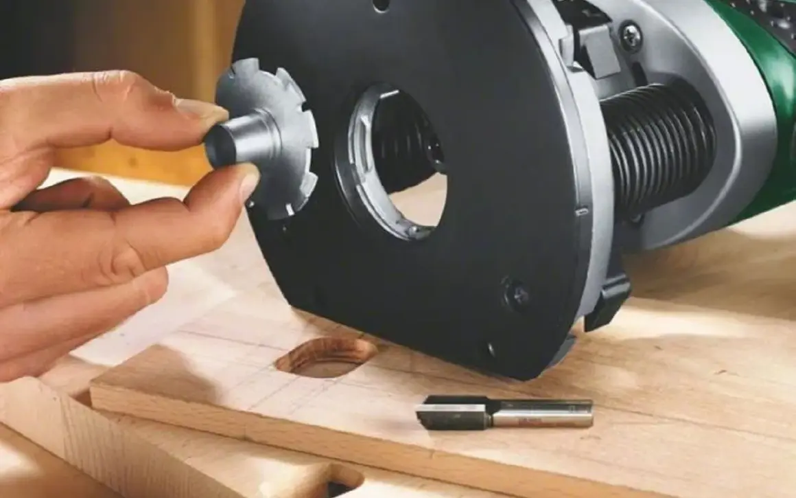 Main d'un artisan ajustant un accessoire sur une défonceuse, pour un choix précis de l'outil. Bois et fraise à portée de main.