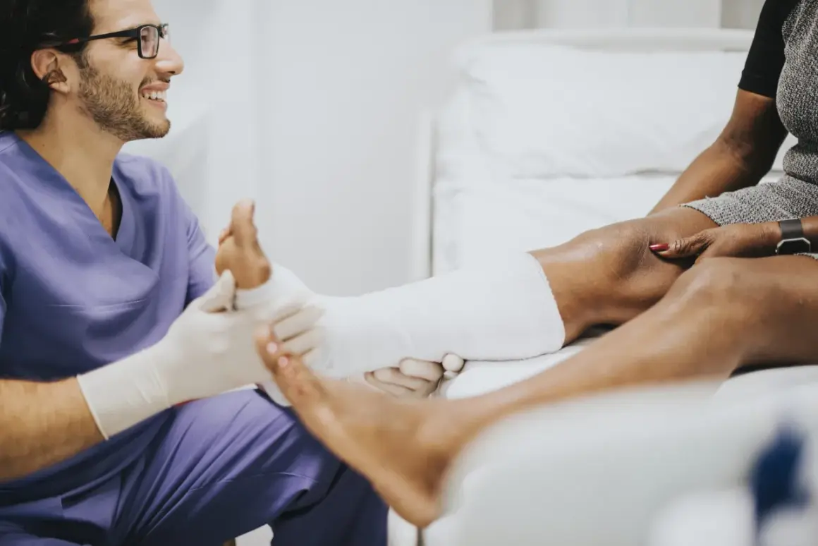 Medico sorridente applica una fasciatura a un paziente con un malleolo gonfio.