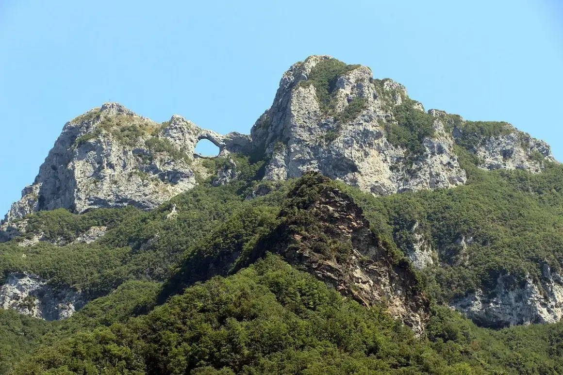Il monte forato, con la sua roccia scolpita dal vento, si erge maestoso tra il verde della vegetazione e l'azzurro del cielo.