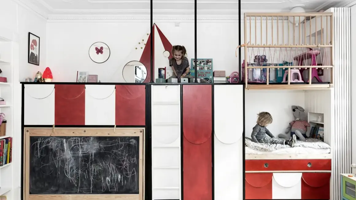 Zwei Kinder teilen sich ein Zimmer mit kreativen Schlafkojen und Spielbereichen. Ein Kind sitzt auf einem Bett, das andere spielt oben.