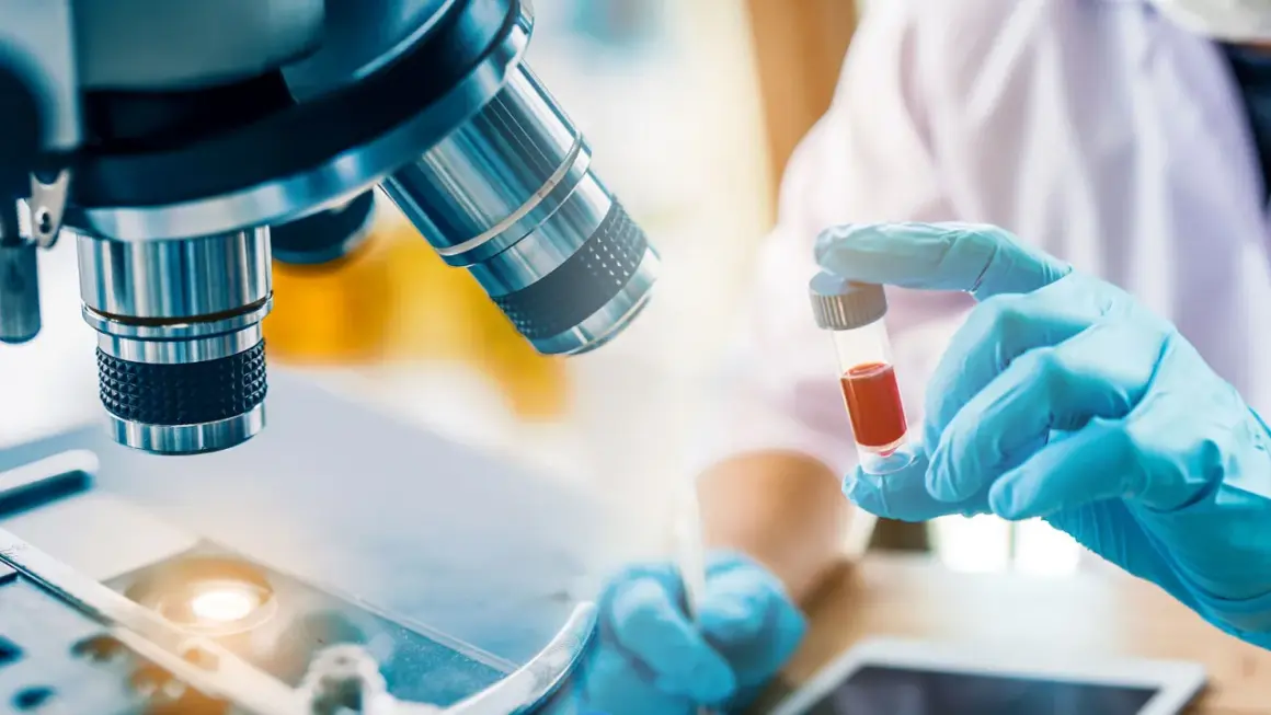 Forscher untersuchen Blutproben für die Immuntherapie bei Lungenkrebs. Ein Mikroskop und eine Ampulle mit roter Flüssigkeit sind zu sehen.