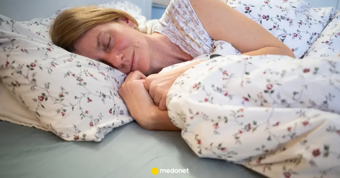 Kobieta zasypia w łóżku, otulona pościelą w kwiaty. To idealny moment na czytanie przed snem.