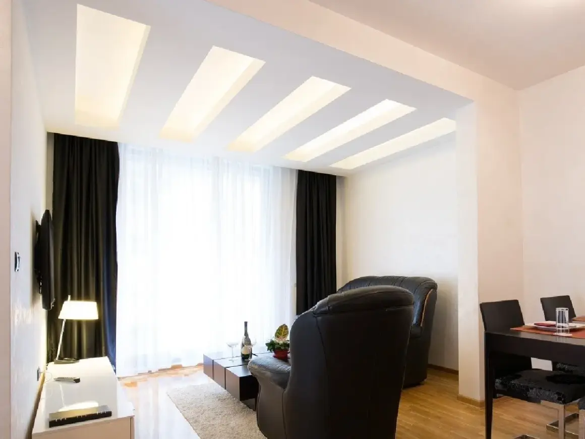 Nowoczesny salon z designerskim plafonem led, który subtelnie rozświetla wnętrze. Drewniane elementy dodają ciepła.