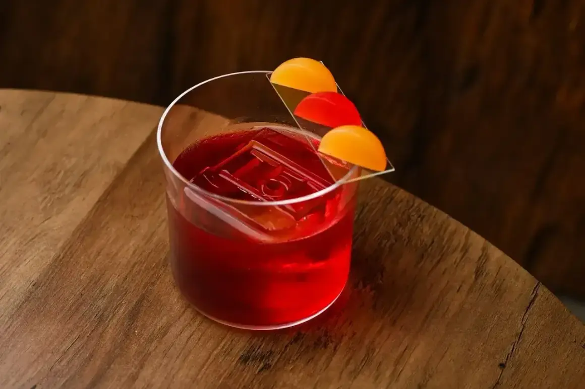 Elegancki Negroni Sbagliato z kostką lodu i ozdobą z pomarańczy i czerwonych owoców na drewnianym blacie.