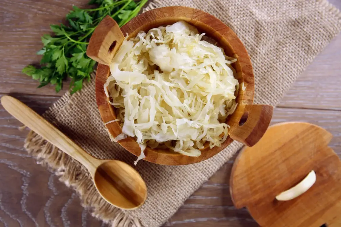 Holzschale mit Sauerkraut, daneben ein Holzlöffel und Petersilie. Sauerkraut gesund und lecker!