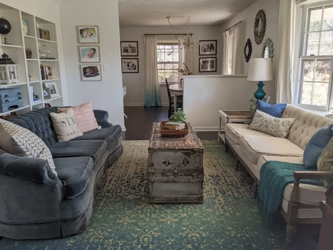A living room with two sofas, a vintage trunk coffee table, and a patterned rug. This space shows how to brighten a dark room with light-colored furniture and ample natural light.
