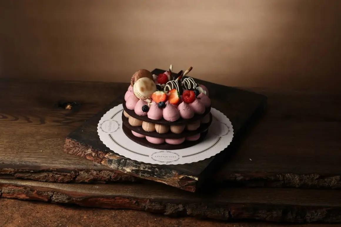 En vacker tårta med macarons, bär och chokladdekorationer, serverad på ett rustikt träfat.