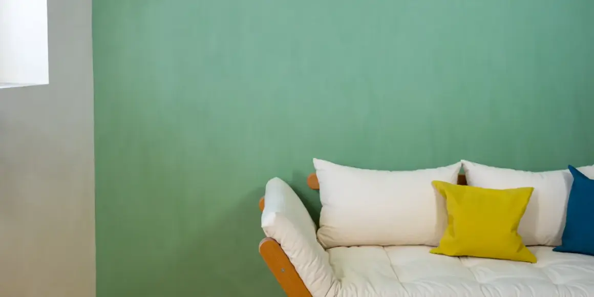 Ein Sofa mit weißen und gelben Kissen vor einer mintgrünen Wand. Die Frage "wieviel Wandfarbe pro qm" wird hier nicht beantwortet.