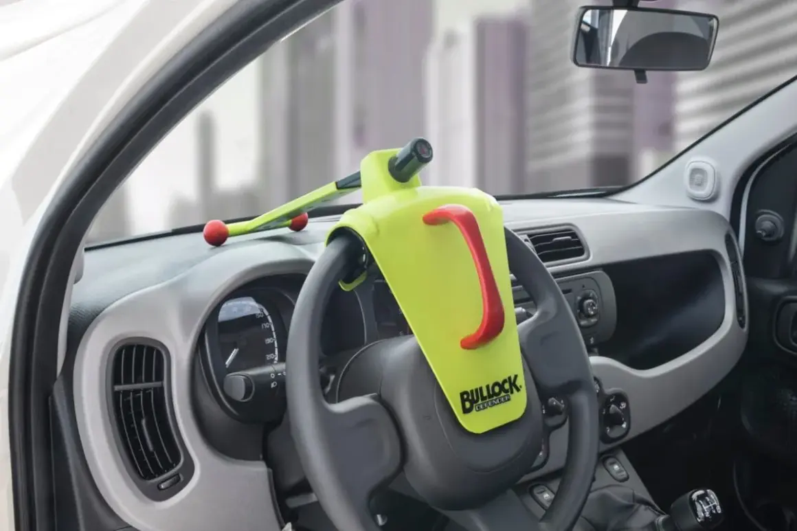 Un antivol de volant Bullock Defender est installé. Il est jaune vif avec une poignée rouge. Il n'y a pas de clé visible, ce qui peut faire penser à comment débloquer un volant sans clé.