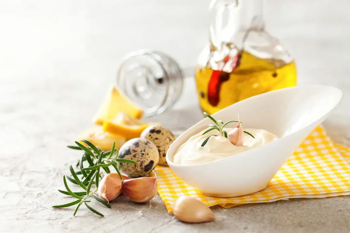 Kremowy sos aioli z czosnkiem i rozmarynem, obok jaj przepiórczych i butelki oliwy.
