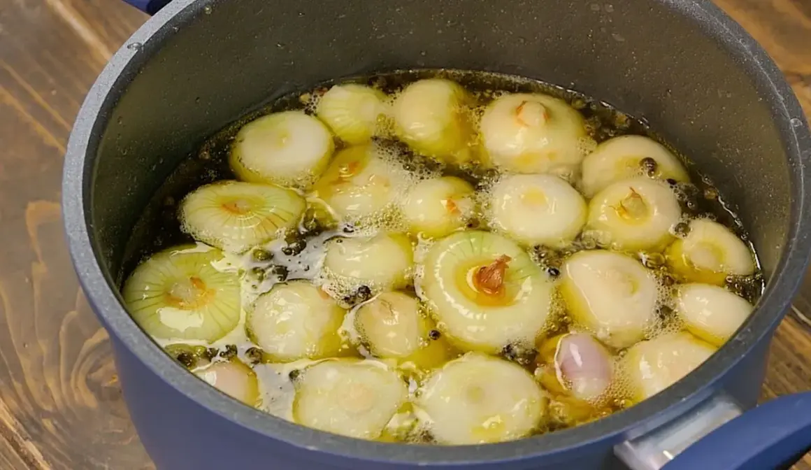 Cipolline in agrodolce in padella con aceto balsamico, che sobbollono in un liquido dorato, pronte per essere gustate.