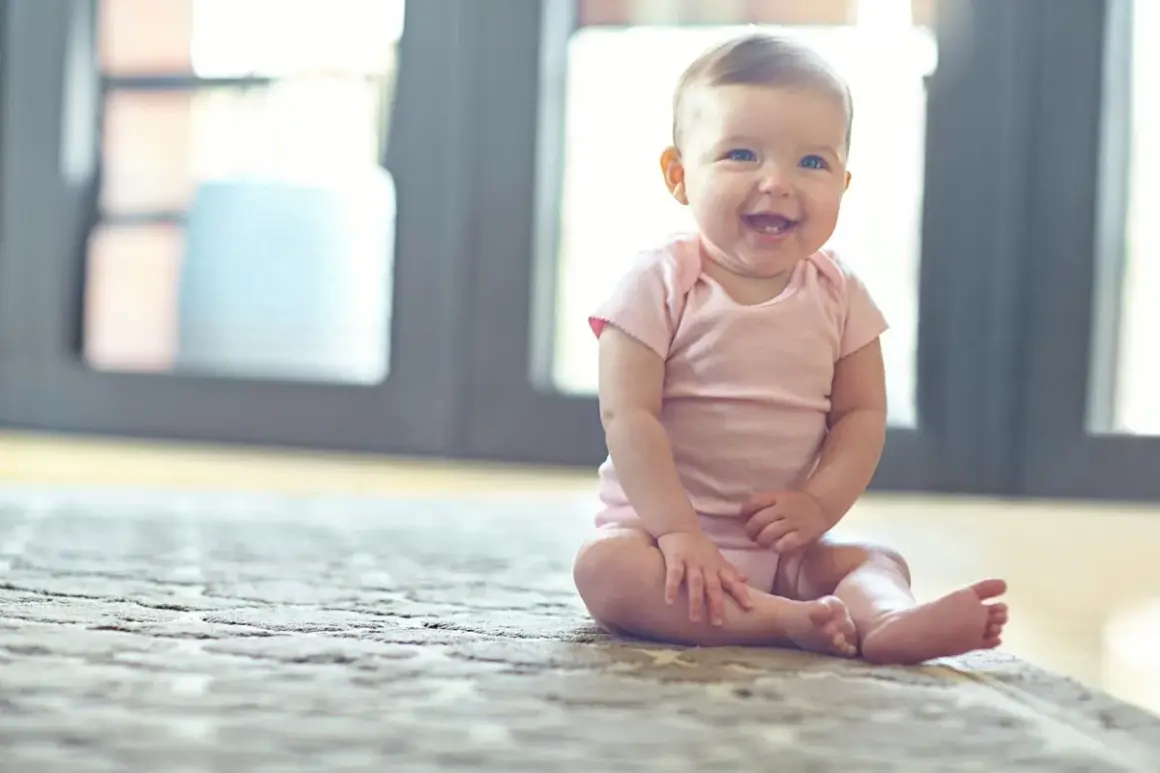 Ein fröhliches Baby sitzt auf einem Teppich und lacht.