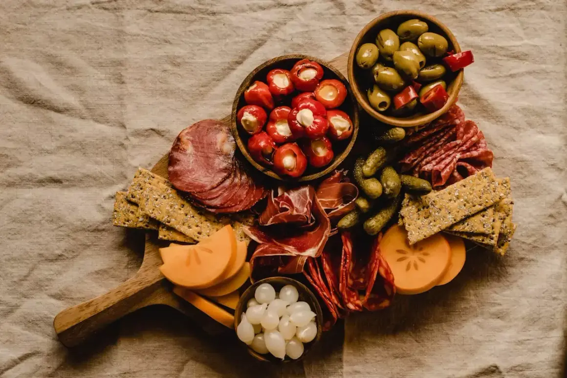 Tabla de que es charcuteria: embutidos, aceitunas, pepinillos, pimientos rellenos, queso y galletas.