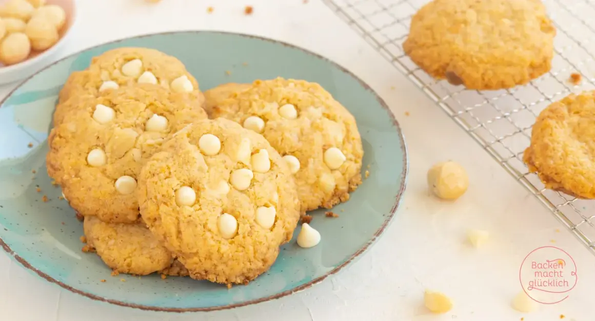 Saftige white chocolate macadamia cookies auf einem türkisfarbenen Teller, daneben Macadamianüsse und Schokostückchen.