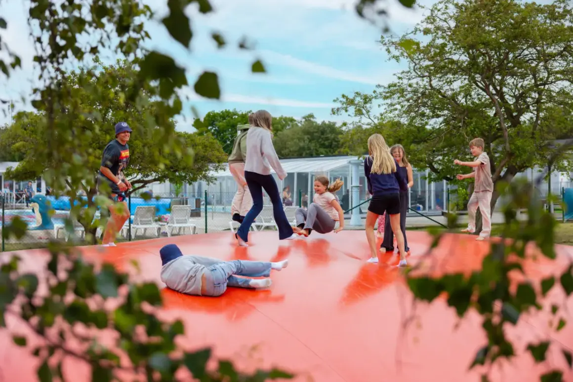 Barn hoppar på en stor orange studsmatta vid first camp råå vallar-helsingborg. Solen skiner och det är en härlig sommardag.