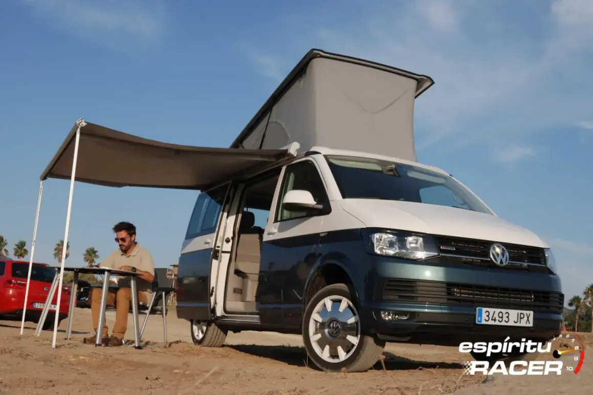 Hombre sentado en mesa plegable bajo toldo de camper en playa, con medidas california beach.