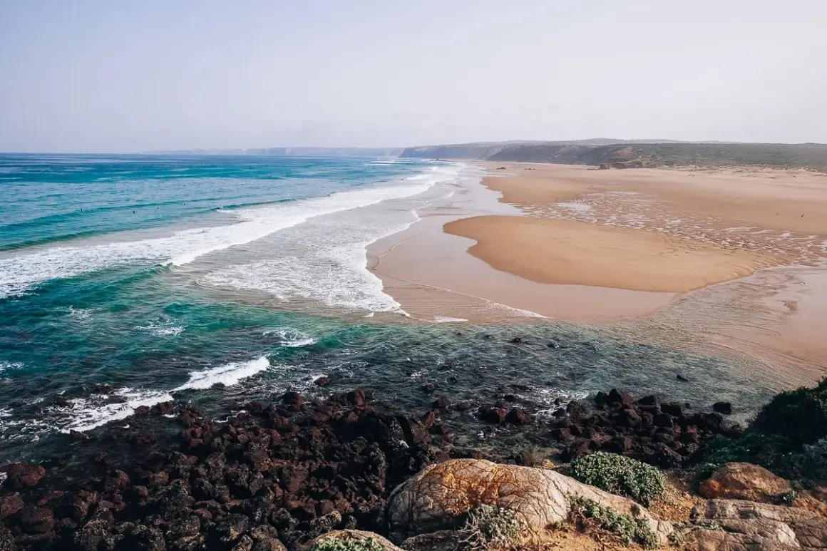 Piękne plaże i turkusowe morze, idealne na algarve wakacje. Surferzy łapią fale, a skały tworzą malowniczy brzeg.