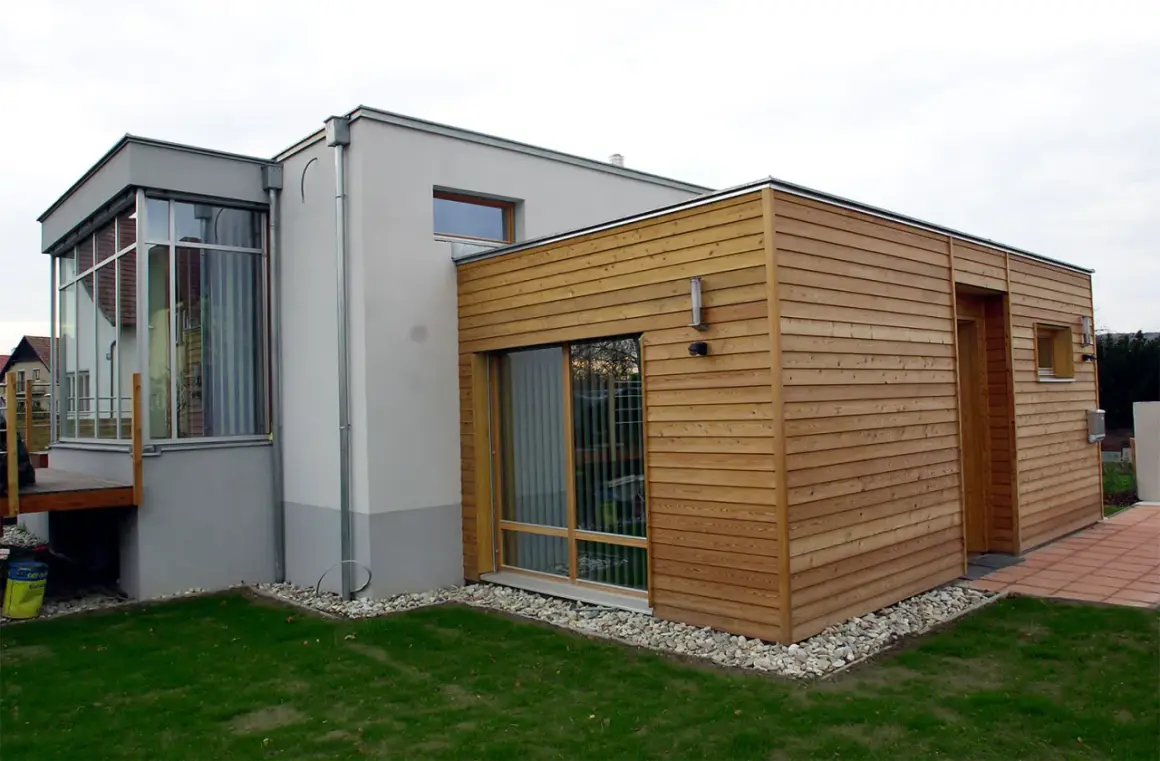 Moderner Anbau an altes Haus: Ein Teil des Hauses ist mit Holz verkleidet, der andere Teil verputzt. Große Fensterfronten und ein Wintergarten.
