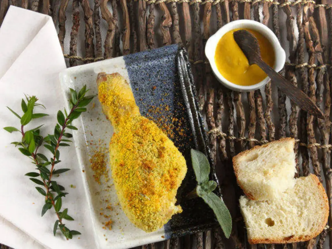 Fusi di pollo al forno dorati e croccanti, serviti con pane fresco, salsa gialla e rametti verdi.