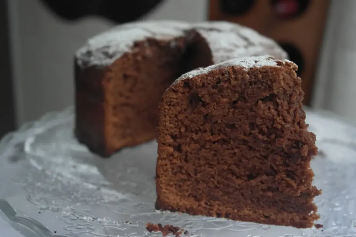 Un trozo de el mejor bizcocho de chocolate del mundo, espolvoreado con azúcar glas, sobre una bandeja de cristal.