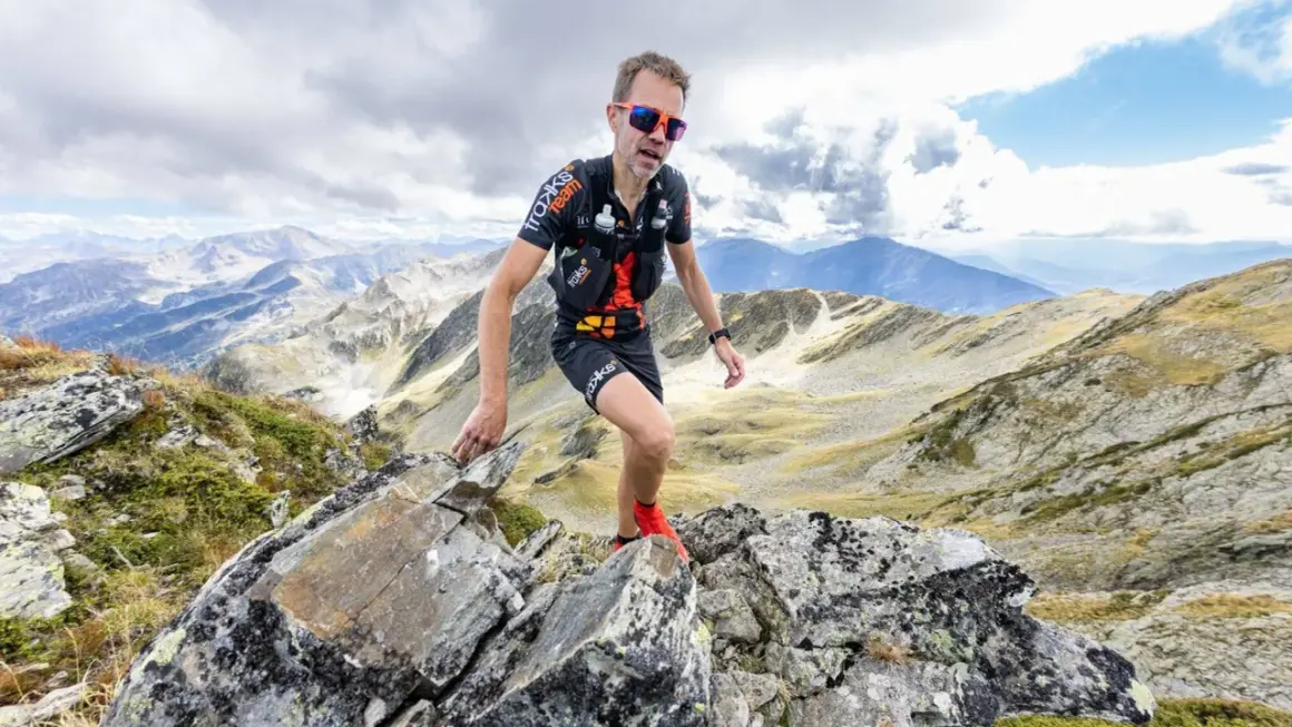 Un traileur en plein effort sur un sentier rocailleux, le regard déterminé, incarne l'ultra spirit dans un paysage montagneux spectaculaire.