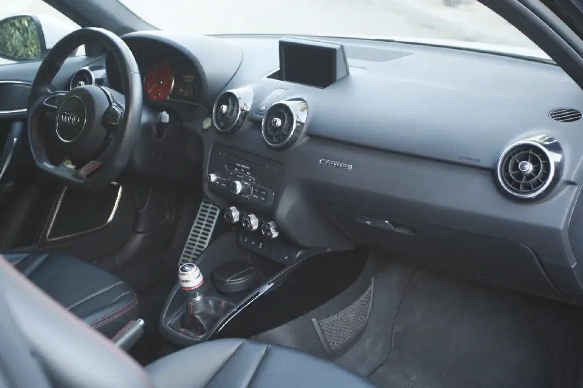 Vue de l'intérieur d'une Audi A1, avec le volant, la console centrale et les sièges en cuir noir.