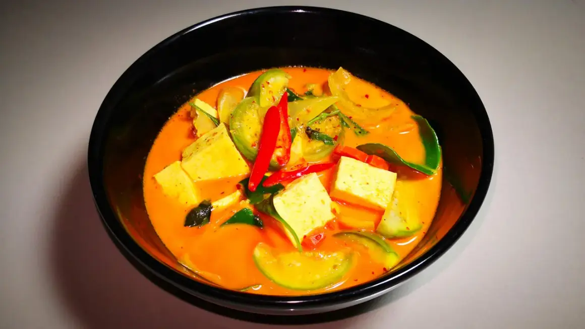 Ein dampfendes rotes Curry mit Tofuwürfeln, grünen Tomaten und scharfen Chilischoten. Dieses rote Curry ist scharf und verlockend.