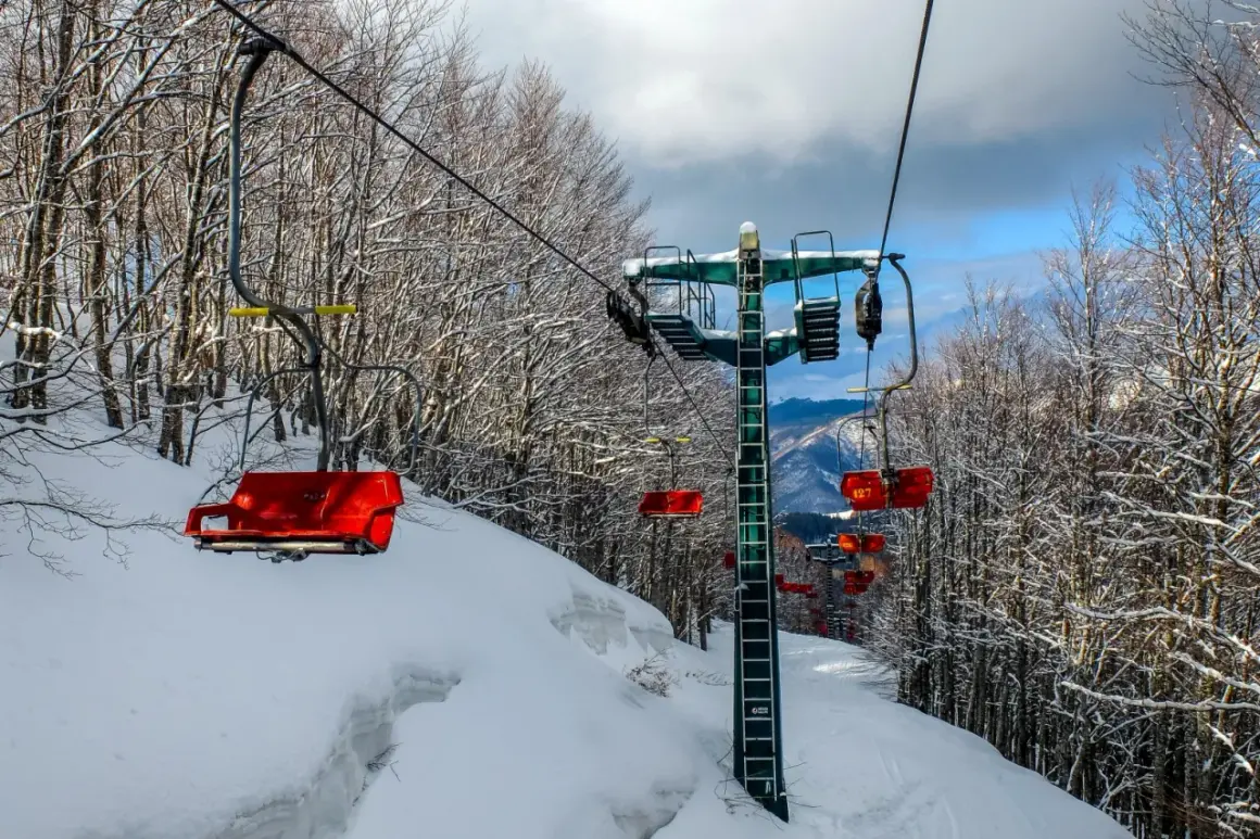 Seggiovia rossa su piste innevate ad Abetone, l'altitudine offre panorami mozzafiato tra alberi spogli coperti di neve.