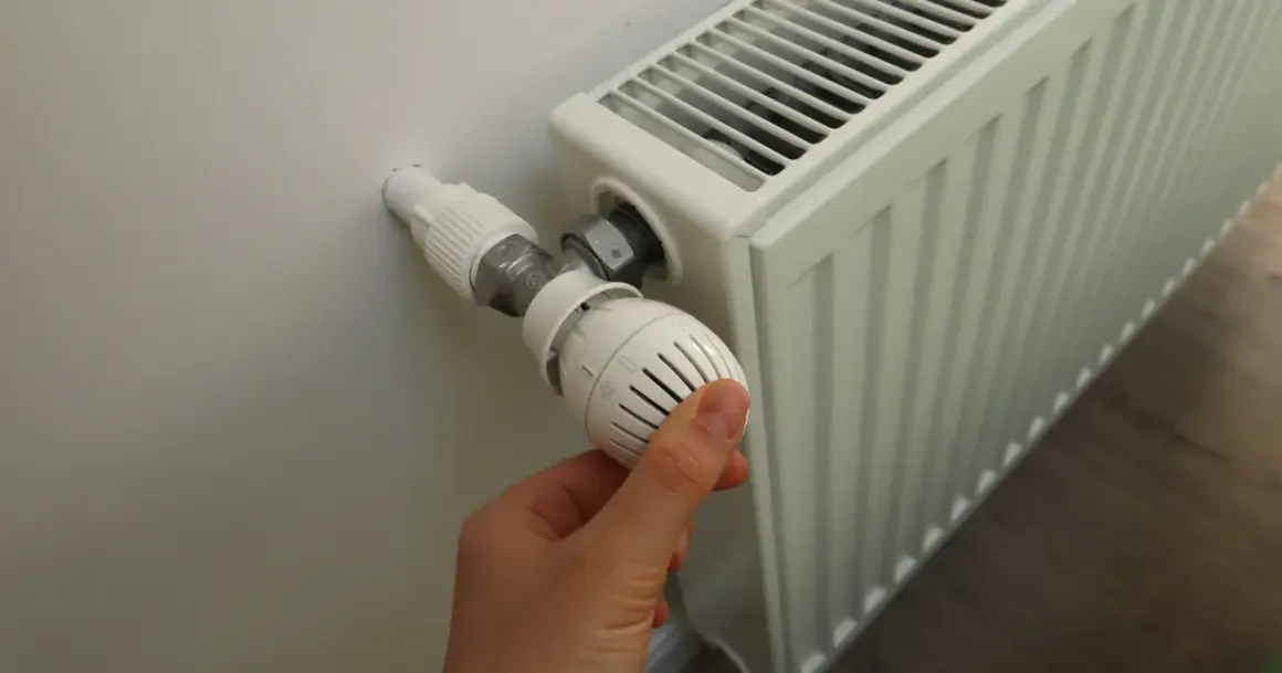 Ręka reguluje termostat grzejnika, gdy zaczynają grzać w blokach.