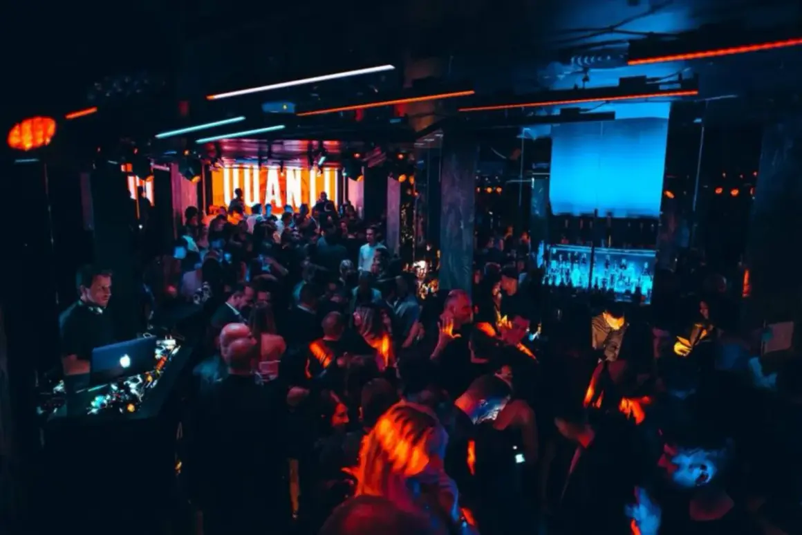 Una folla balla in una discoteca illuminata da luci al neon, un DJ suona musica elettronica. Sembra una delle migliori discoteche techno in Italia.