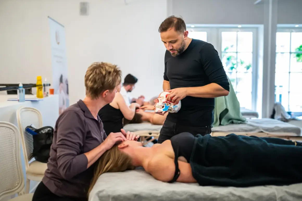 Masaż twarzy: terapeuta pokazuje model czaszki, druga osoba masuje twarz pacjentki.